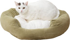 A white cat with black patches lies inside a round, cushioned pet bed with an olive green velvet exterior and a white faux fur lining, set against a plain white background.