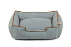A rectangular dog bed with a blue and white striped fabric, featuring a raised cushioned interior and a contrasting brown leather trim, shown on a plain white background.