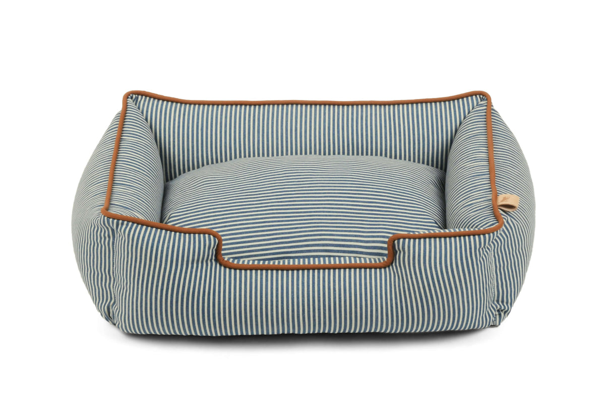 A rectangular dog bed with a blue and white striped fabric, featuring a raised cushioned interior and a contrasting brown leather trim, shown on a plain white background.