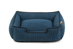 A blue striped pet bed with black piping and a small tan tag on the side, photographed on a clean white background.