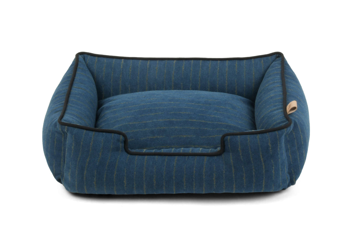 A blue striped pet bed with black piping and a small tan tag on the side, photographed on a clean white background.